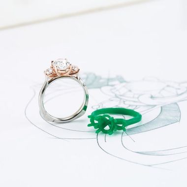 A finished diamond engagement ring photographed over its original hand-drawn design sketch